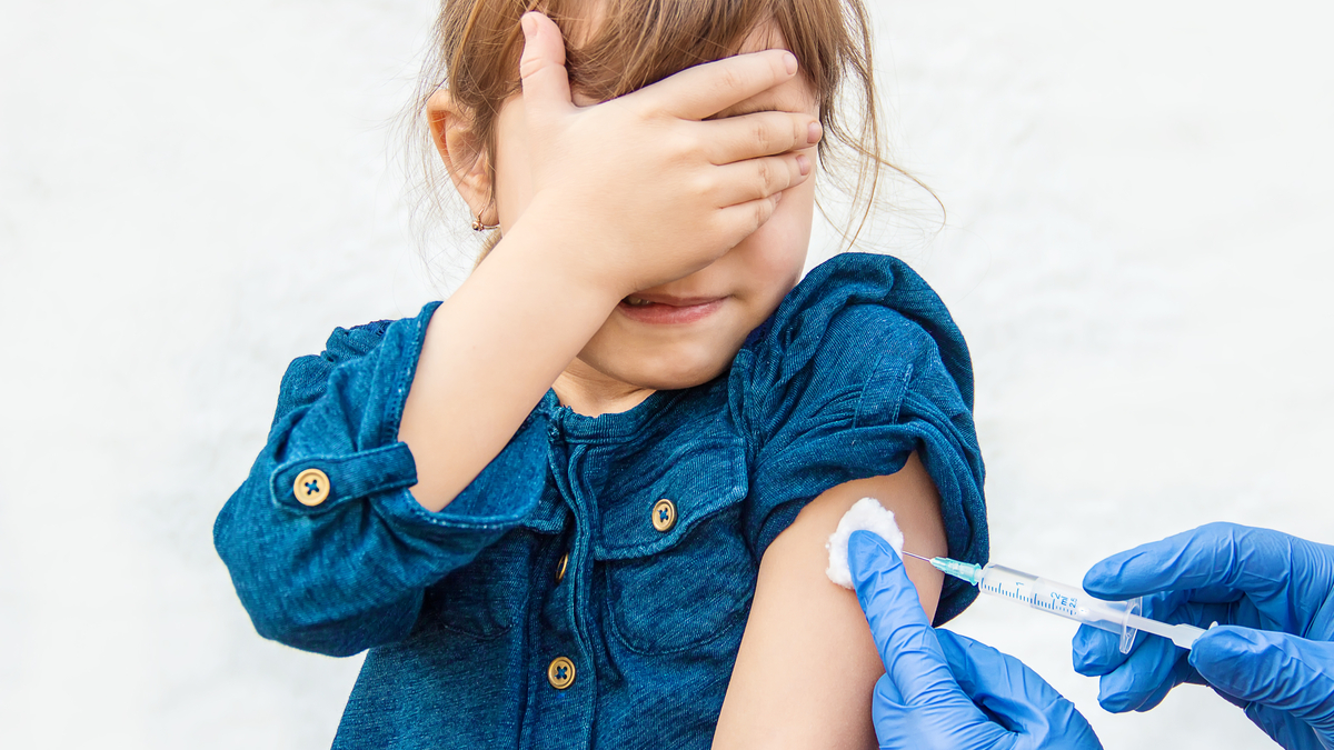 A photo of a young girl covering her eyes while receiving a shot.