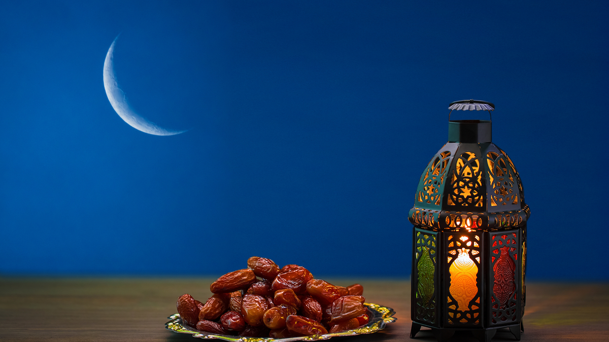 Picture of dates and Ramadan lamp against a silhouette of a sliver of the moon.