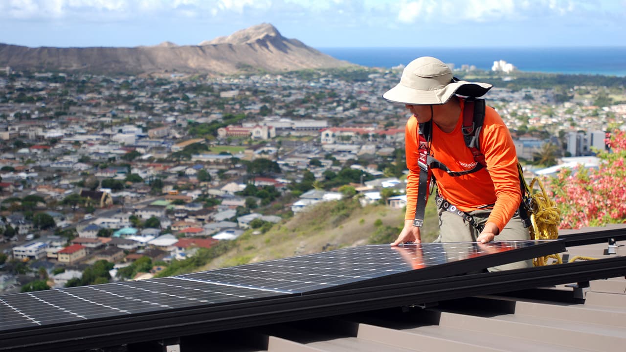 Photo of Dane Hew Len, lead installer for RevoluSun, placing a solar panel on a roof
