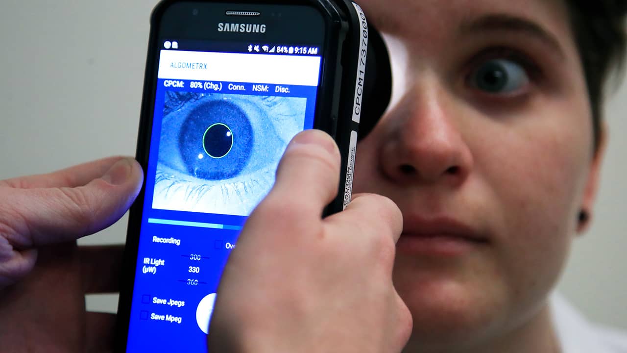 Photo of Clinical Research Assistant Kevin Jackson using AlgometRx Platform Technology on Sarah Taylor's eyes to measure her degree of pain