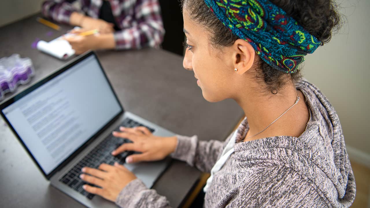 Photo of a female high school student using her laptop to access an online school