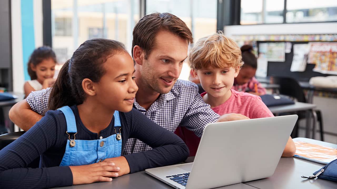 Photo of male teacher working closely with his students around a laptop