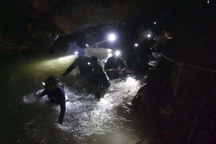 Rescue team in Thailand looking for young soccer players and their coach walk through a cave.