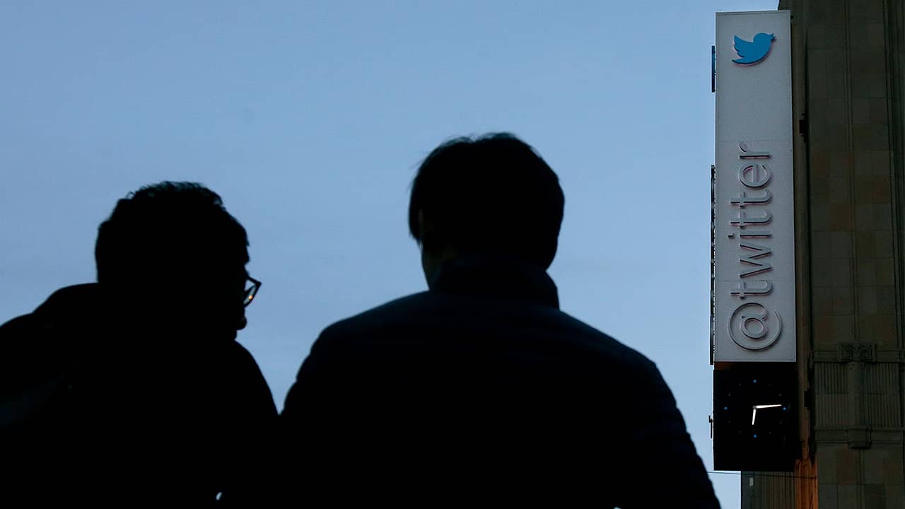 Photo of two men waiting to cross the street under a sign at Twitter headquarters in San Francisco