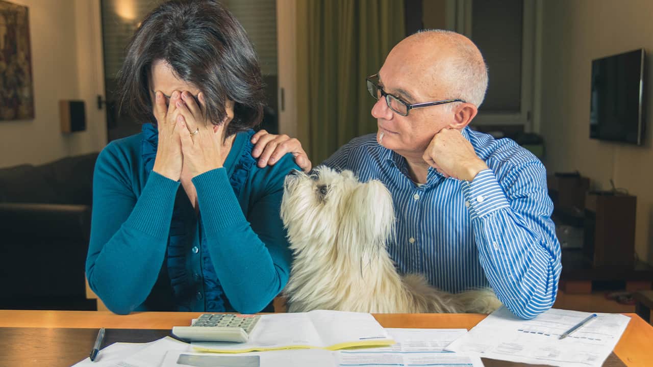 A worried wife and husband with pet dog sitting at a table with piles of billsman 