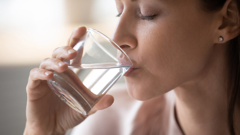 Image of a woman facing left and drinking water from a clear glass