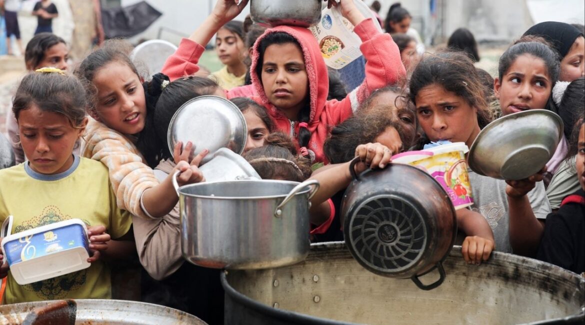 Palestinians wait to receive food cooked by a charity kitchen, in Nuseirat, central Gaza Strip, April 8, 2025. REUTERS/Ramadan Abed