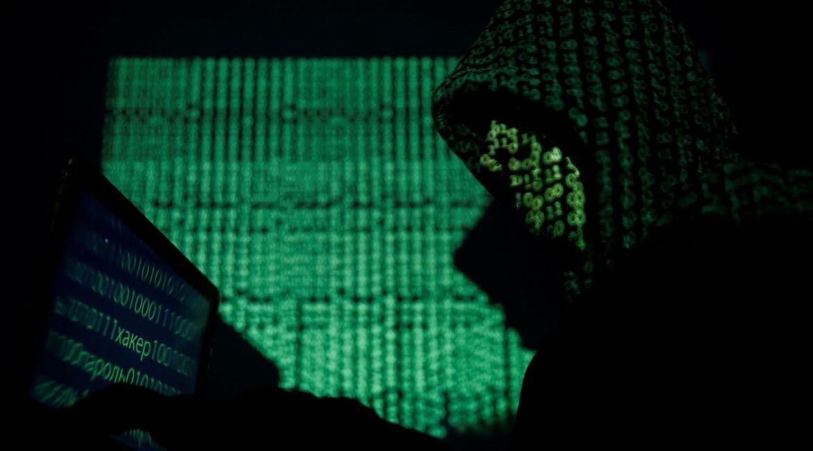 A hooded man holds a laptop computer as cyber code is projected on him in this illustration picture taken on May 13, 2017. (Reuters File)