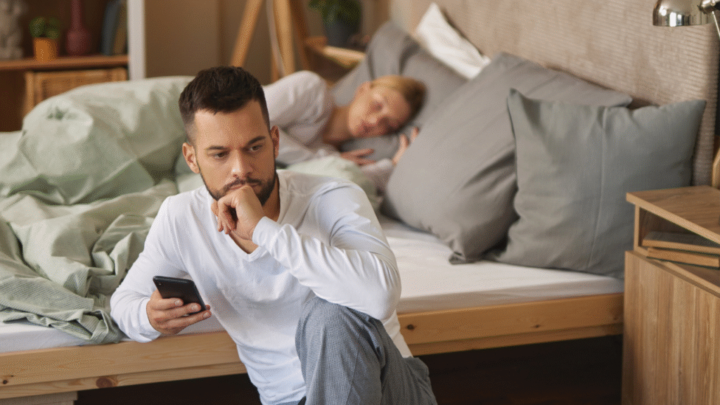 Man with smart phone in bedroom, woman sleeping in the background