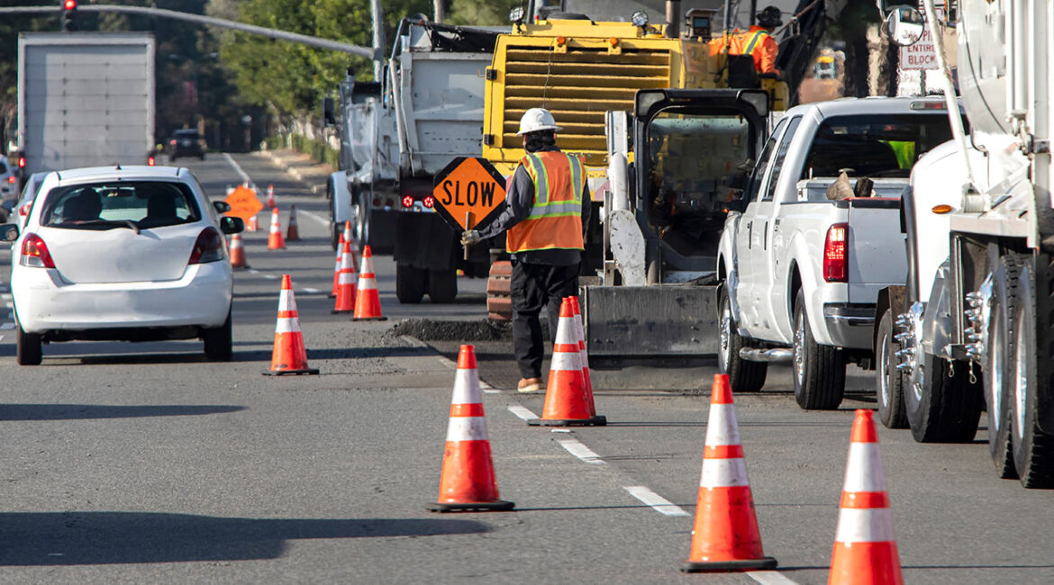 Wide view of road construction site and a man holding traffic sign that says SLOW .Bright orange traffic cones and trucks and cars are visible Asset id: 1624463698 Wide view of road construction site and a man holding traffic sign that says SLOW .Bright orange traffic cones and trucks and cars are visible