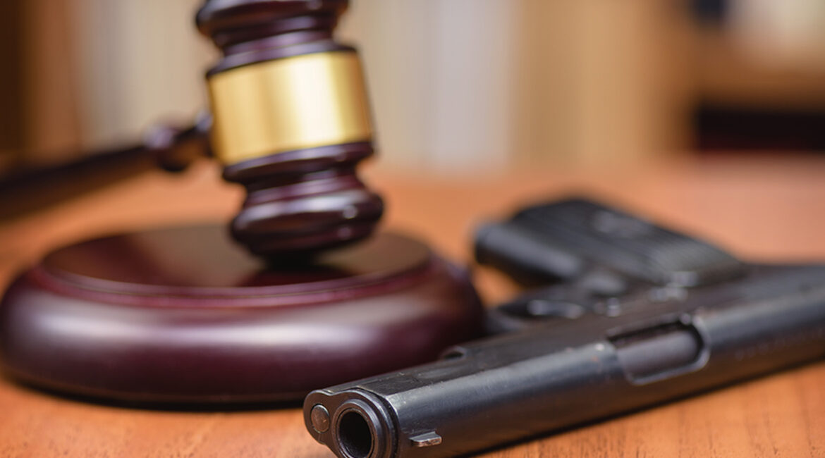 Court for the illegal use of weapons. Sentence for murder. Judge's gavel on wooden table. Judge, hammer, pistol on wooden background.