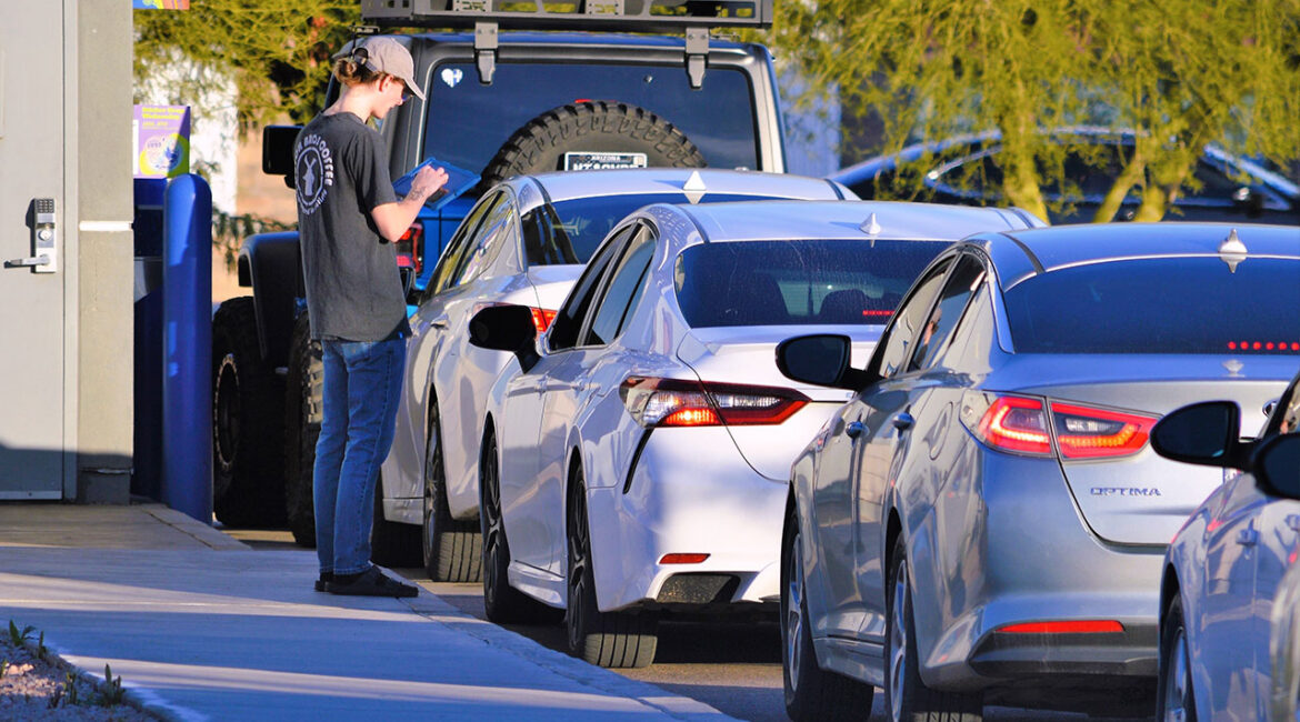 A Dutch Bros Coffee employee takes customers drink orders at cars lined up at a drive-thru.