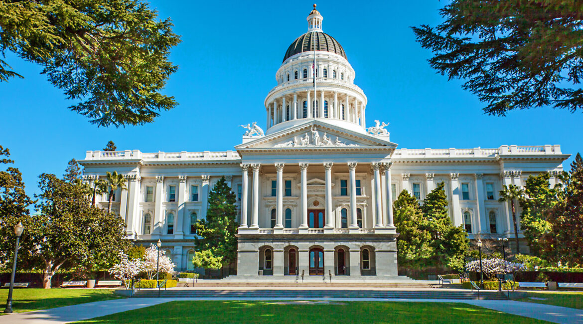 California State Capitol building in Sacramento, USA, framed by trees on a clear blue day.