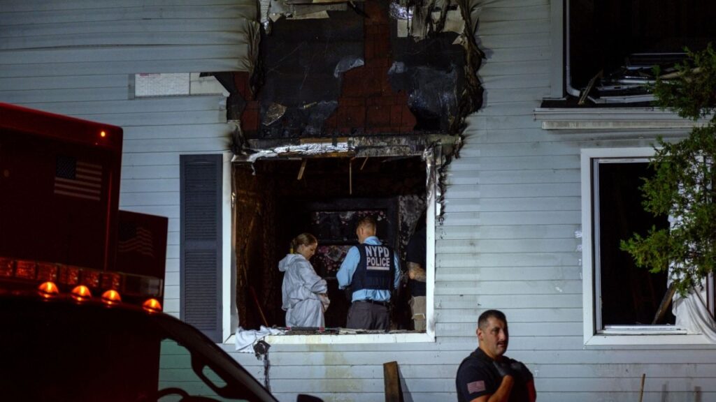 Investigators at the scene of a fire in the Bellerose neighborhood of Queens shortly after midnight on Tuesday morning, Sept. 9, 2025. A 77-year-old man and 78-year-old woman were discovered dead inside the home on Monday after a man entered the house and set it ablaze, according to the police. (Dakota Santiago/The New York Times)