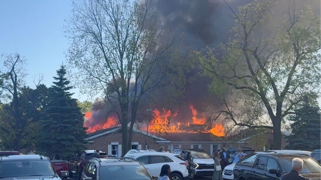 People gather at the site as smoke and fire rise, following an incident in which a man crashed his vehicle through the front doors of a Michigan church and opened fire with an assault rifle and set the church ablaze, in Grand Blanc, Michigan, U.S., September 28, 2025, in this screengrab obtained from social media video. Heem Vaniawala/via REUTERS