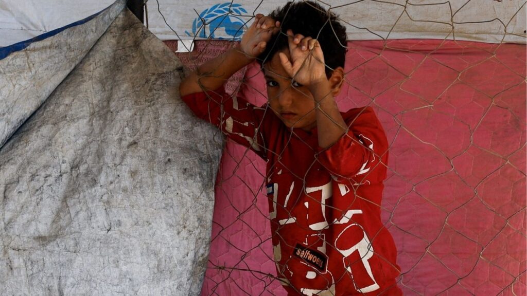 A displaced Palestinian child, who fled Gaza City due to an Israeli military operation, stands by a fence, as he rests on the roadside, in the central Gaza Strip, October 5, 2025. (Reuters/Mahmoud Issa)