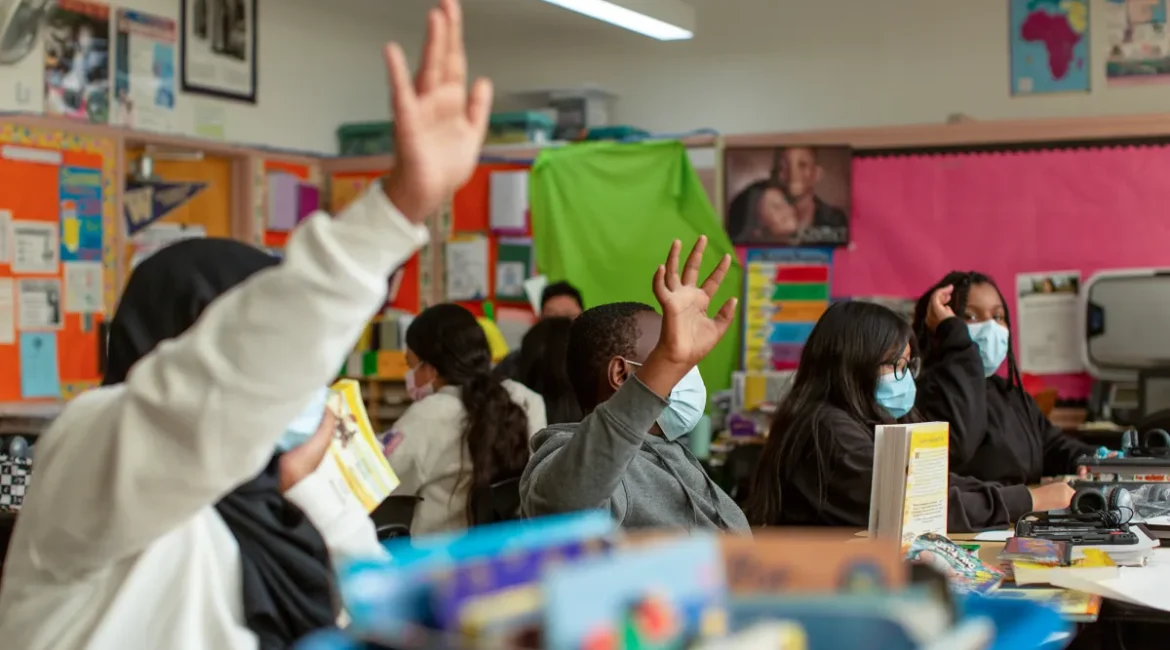 Image of students raising their hands in a brightly color classroom