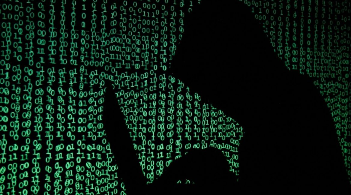 A hooded man holds a laptop computer as cyber code is projected on him in this illustration picture taken on May 13, 2017. (Reuters File)