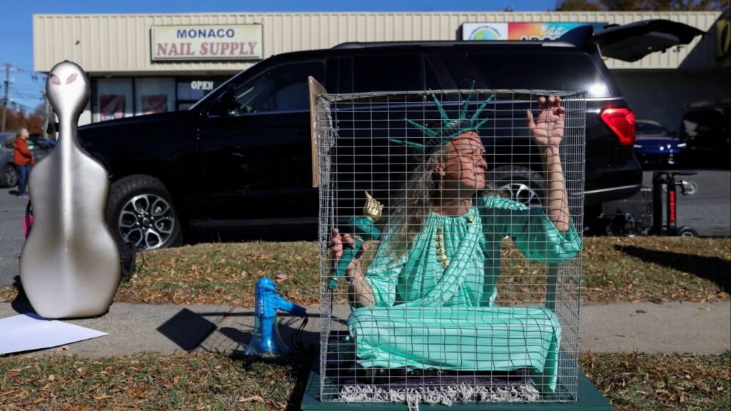 Shana Blake, a protestor wearing a Statue of Liberty outfit sits in a cage, as Members of the Customs and Border Patrol (CBP) conduct immigration raids on the streets of Charlotte, North Carolina, U.S., November 17, 2025. (Reuters/Sam Wolfe)