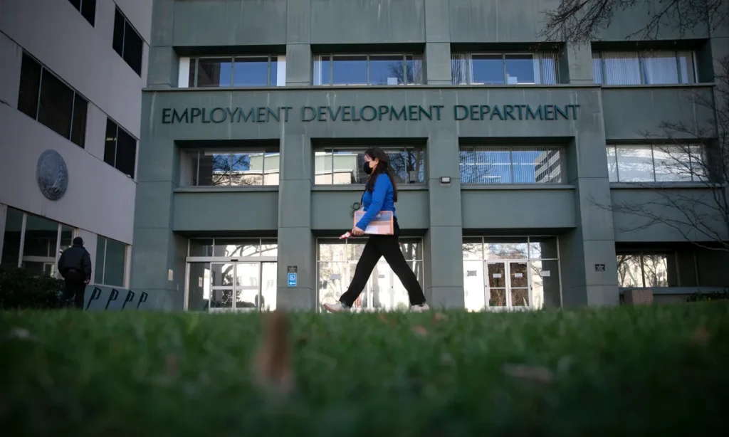 Image of woman in a blue top and black pants walking in front of the state Employment Development Department in Sacramento on a winter day.