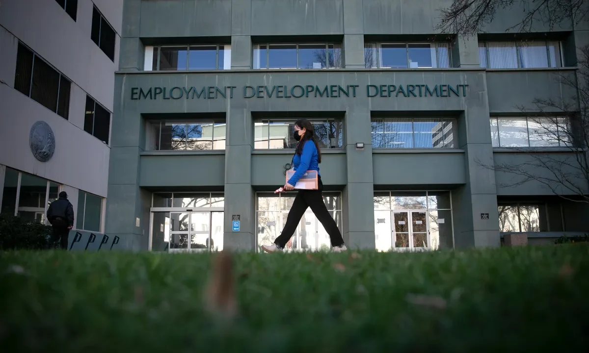 Image of woman in a blue top and black pants walking in front of the state Employment Development Department in Sacramento on a winter day.