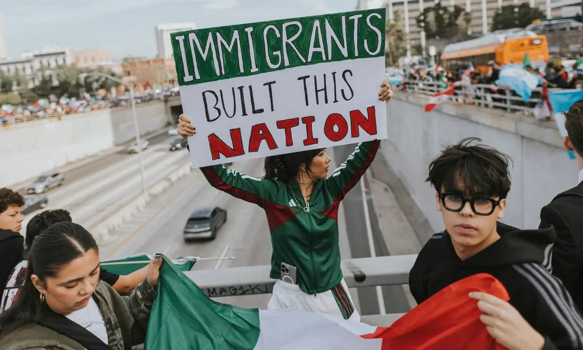 Image of protesters holding an "Immigrants Built This Nation" sign while standing on a Freeway 101 overpass