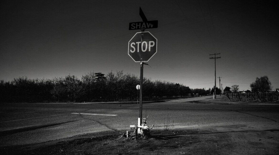 Black and white photo illustration of a deadly Fresno County intersection, its stop sign, and a white cross memorial with flowers there