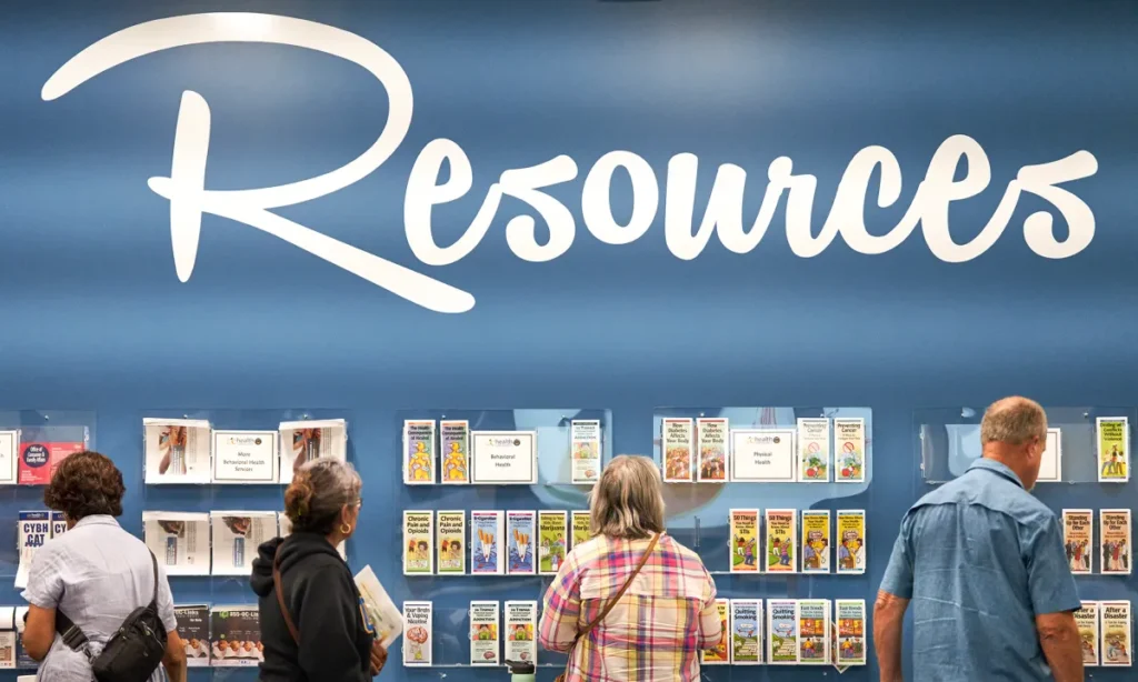 Image of people checking out mental health services brochures on racks beneath a white Resources sign against a blue wall