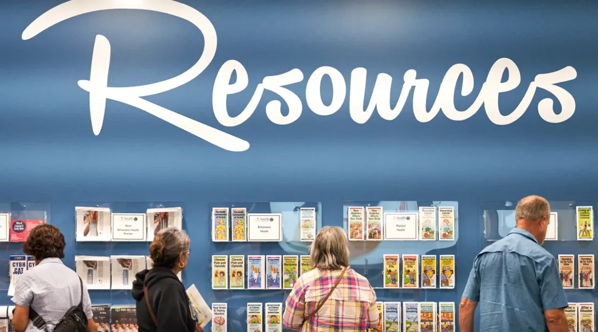 Image of people checking out mental health services brochures on racks beneath a white Resources sign against a blue wall