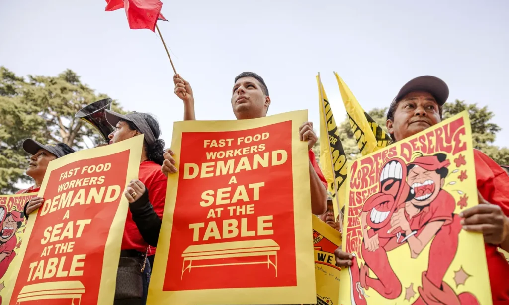 Image of three California fast food workers rallying for a $20 hourly minimum wage. Their signs are red and yellow