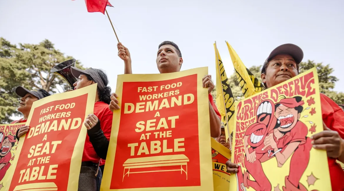 Image of three California fast food workers rallying for a $20 hourly minimum wage. Their signs are red and yellow