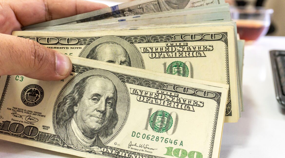 Image of a hand fanning out a stack of $100 bills