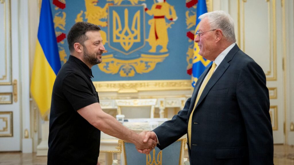Image of Ukraine's President Volodymyr Zelenskiy, in a black shirt, shaking hands with U.S. Special Envoy for Ukraine Keith Kellogg. Kellogg is wearing a dark suit, white shirt, and yellow tie.