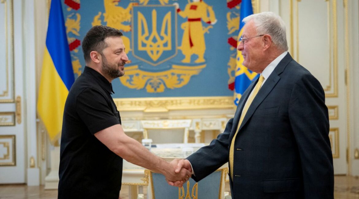 Image of Ukraine's President Volodymyr Zelenskiy, in a black shirt, shaking hands with U.S. Special Envoy for Ukraine Keith Kellogg. Kellogg is wearing a dark suit, white shirt, and yellow tie.