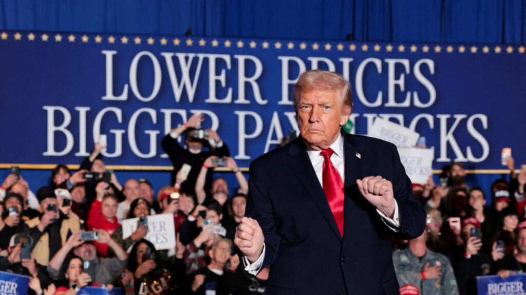 Image of President Donald Trump in dark suit with white shirt and red tie speaking to a crowd at his rally