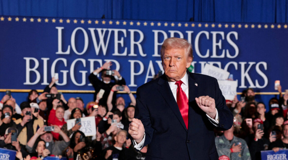 Image of President Donald Trump in dark suit with white shirt and red tie speaking to a crowd at his rally