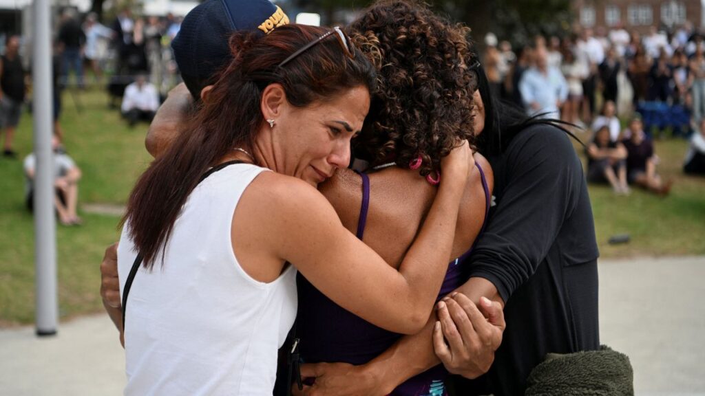 Image of four people embracing at a funeral for victims of a mass shooting in Australia
