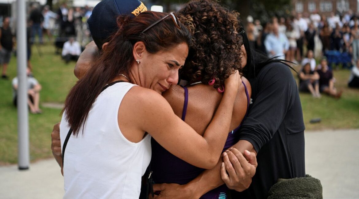 Image of four people embracing at a funeral for victims of a mass shooting in Australia