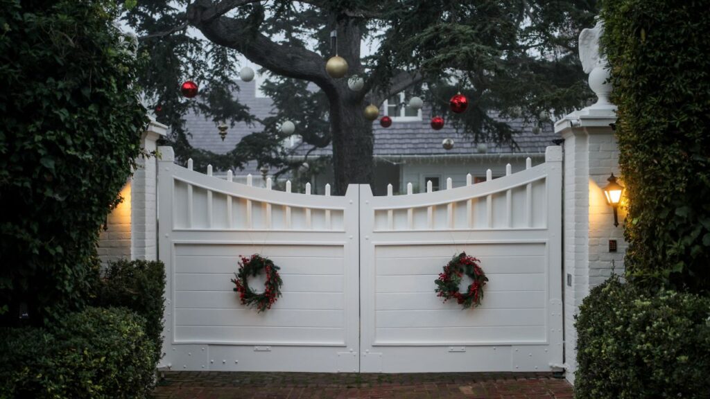 Image of an entrance to the home of slain movie producer and actor Rob Reiner, The entrance is a white gate and Christmas ornaments hang from a tree on the grounds