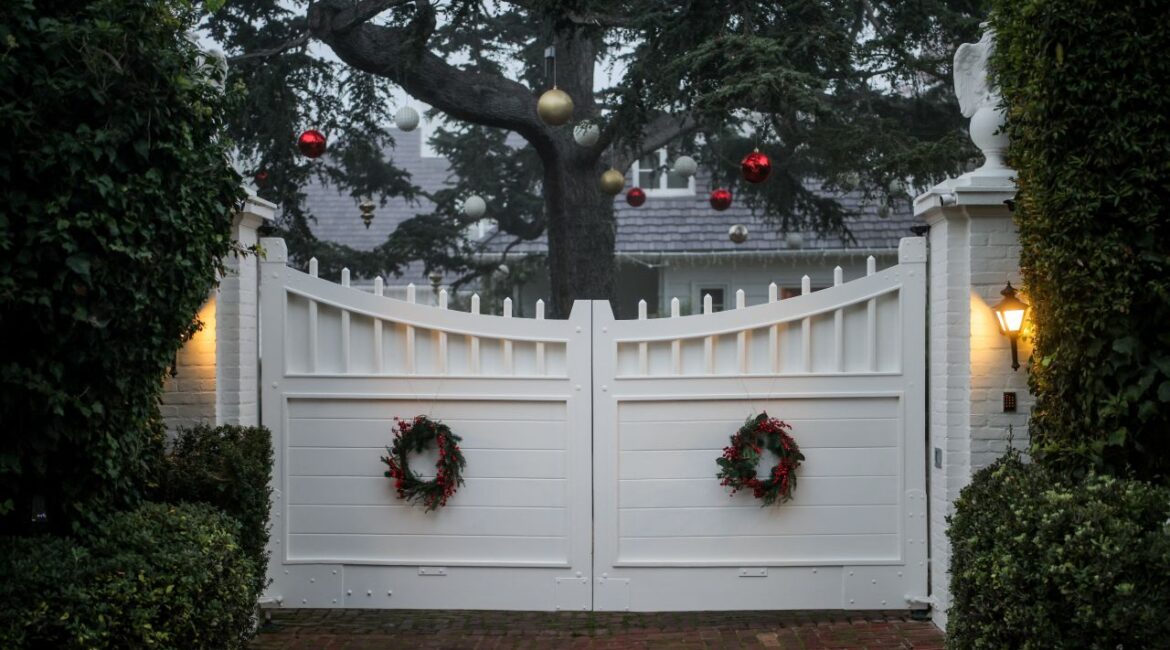 Image of an entrance to the home of slain movie producer and actor Rob Reiner, The entrance is a white gate and Christmas ornaments hang from a tree on the grounds