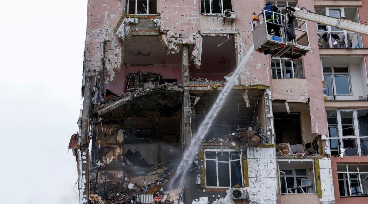 Image of a firefighter on an elevated lift dousing embers at a Ukrainian apartment building hit by Russian drones.