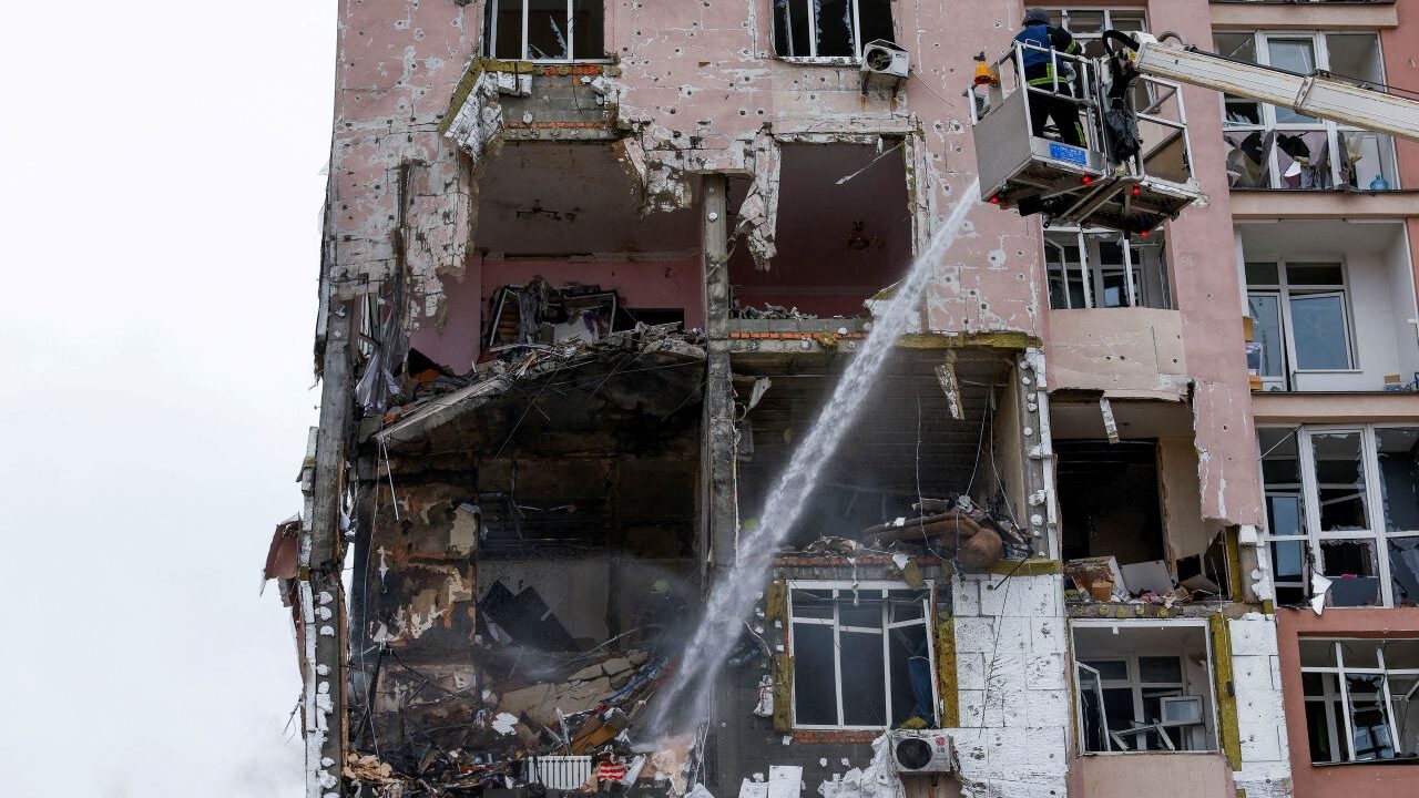 Image of a firefighter on an elevated lift dousing embers at a Ukrainian apartment building hit by Russian drones.