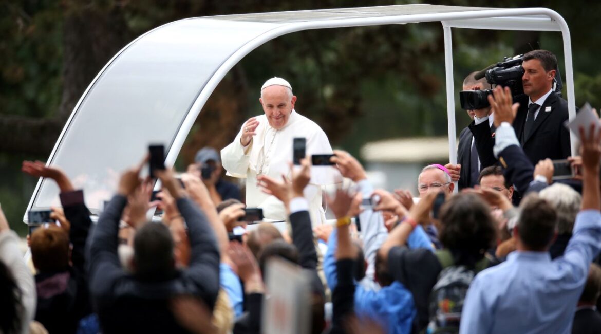 Image of Pope Francis blessing the crowd, which is raising cell phones to video the pontiff.