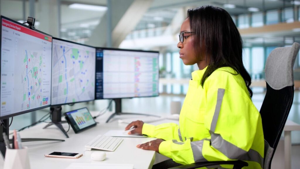 Image of a young Black woman in a yellow windbreaker working at a 911 call center