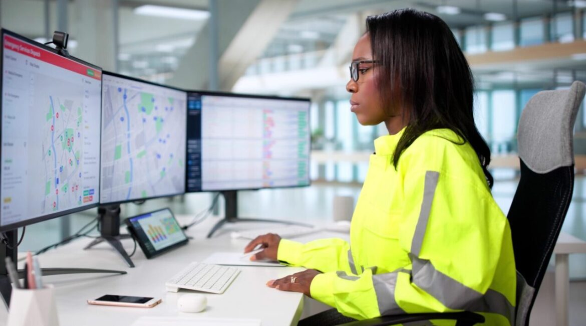Image of a young Black woman in a yellow windbreaker working at a 911 call center