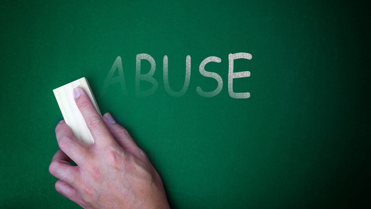 Image of a hand holding an eraser wiping away the word "Abuse" on a green chalkboard