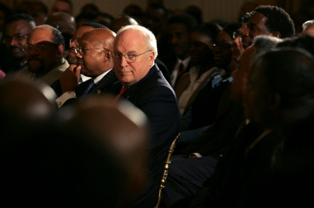 Image of Dick Cheney with his trademark countenance looking across the row in a crowded room.