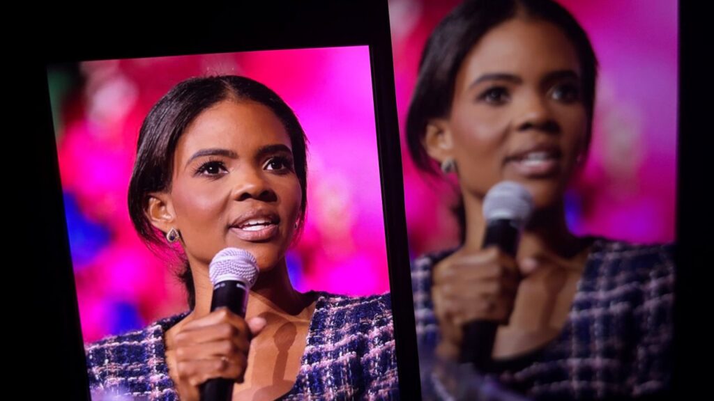Images of Candace Owens speaking to an audience projected on screens in a room