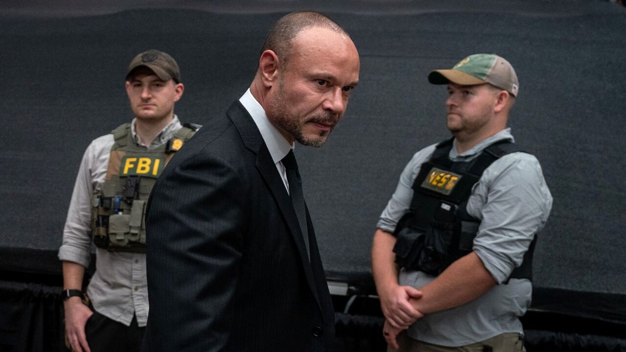 Image on FBI Deputy Director Dan Bongino in a dark suit flanked by FBI agents in bullet proof vests
