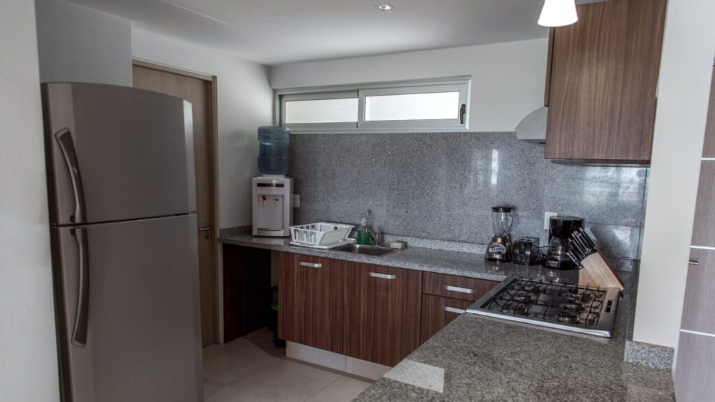 Image of Contemporary apartment kitchen featuring stainless steel refrigerator, granite countertops, dark wood cabinets, gas stove, water dispenser, and breakfast bar in clean residential interior.